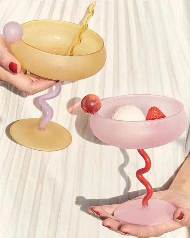Two hands holding a yellow and pink bowl with a spiral handle, one filled with ice cream and strawberries.