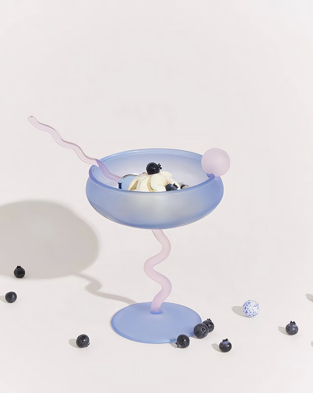 Pastel blue cocktail glass with pink straw and banana slice on a white background