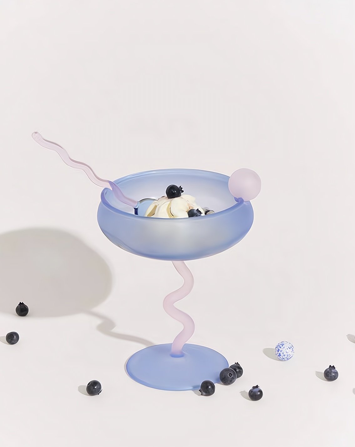 Pastel blue cocktail glass with pink straw and banana slice on a white background
